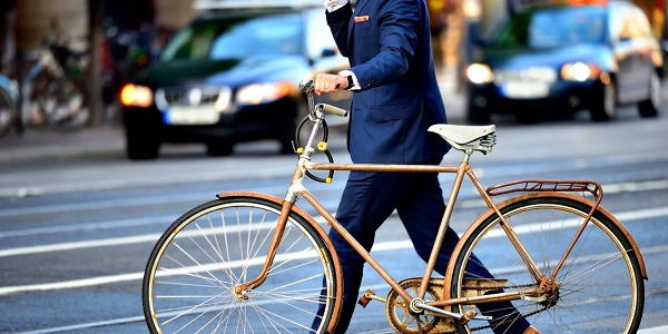 Man wearing suit is walking a bike across the street