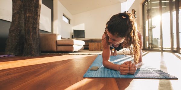 Young woman exercising at home doing a plank and looking at her mobile phone.